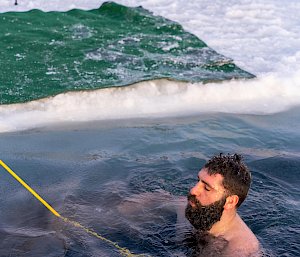 A man floating in a hole in the sea ice. He is attached to a rope.