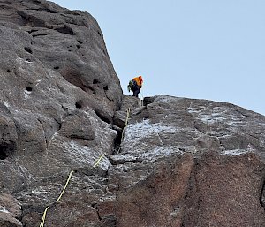 An expeditioner at the top of a bare rock wall while climbing a mountain in Antarctica