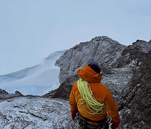 An expeditioner on top of a mountain in Antarctica, backed by cloud.