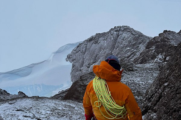 An expeditioner on top of a mountain in Antarctica, backed by cloud.