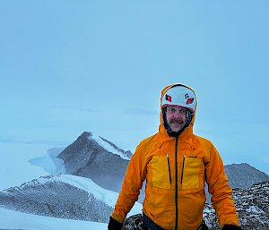 An expeditioner on top of a mountain in Antarctica, backed by cloud.