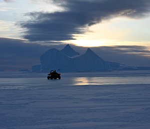 quad bike on sea ice with iceberg in background