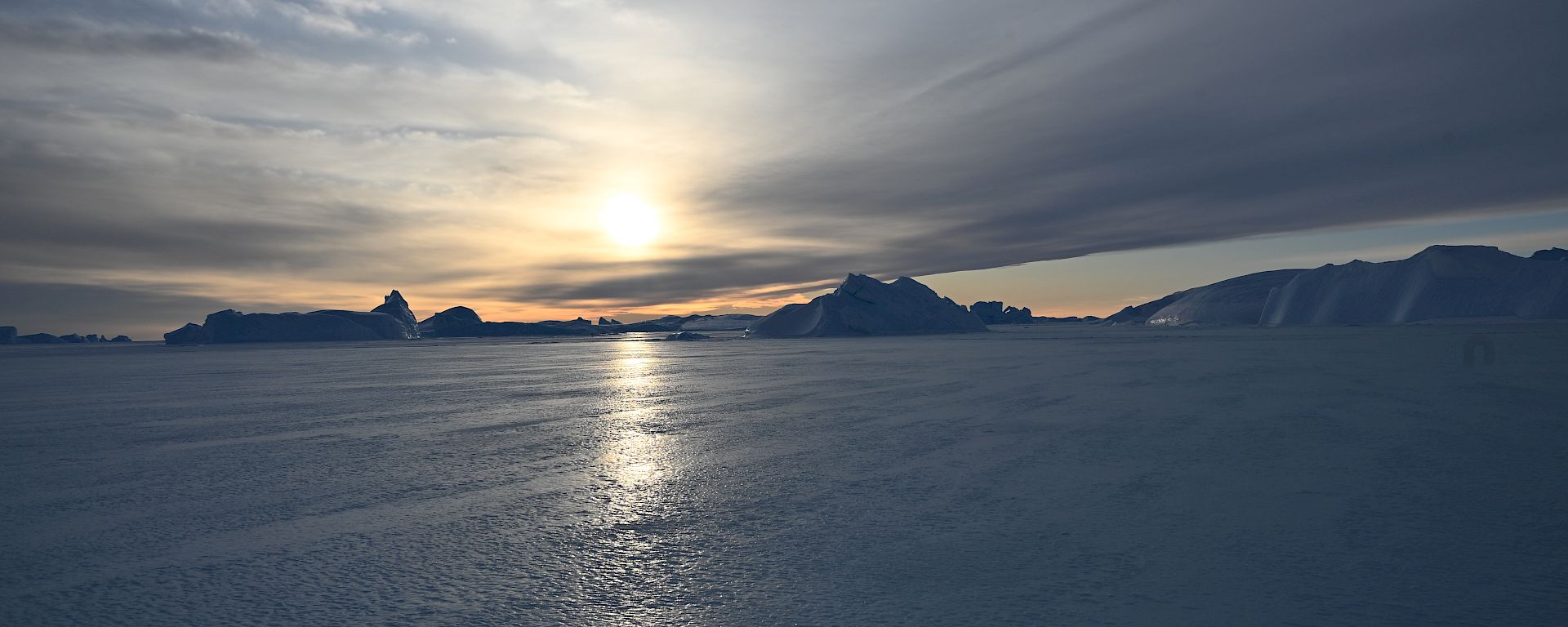 sun setting in background with icebergs in distance