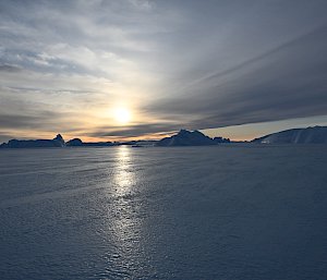 sun setting in background with icebergs in distance