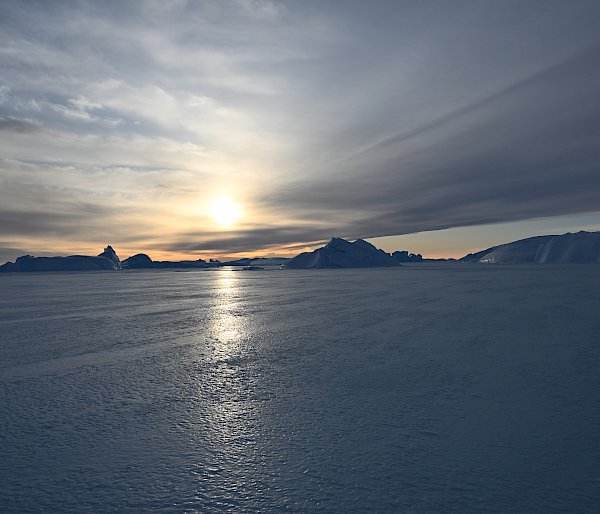 sun setting in background with icebergs in distance