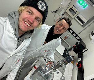 Two men in white lab coats in front of a piece of scientific equipment