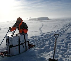 A person pushing a box on a sled in the snow.