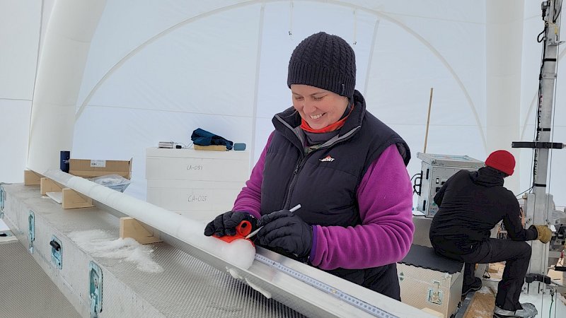 A woman marks the end of an ice core with a pencil.