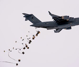 Boxes of supplies being dropped from the rear of a C-17 Globemaster aircraft.