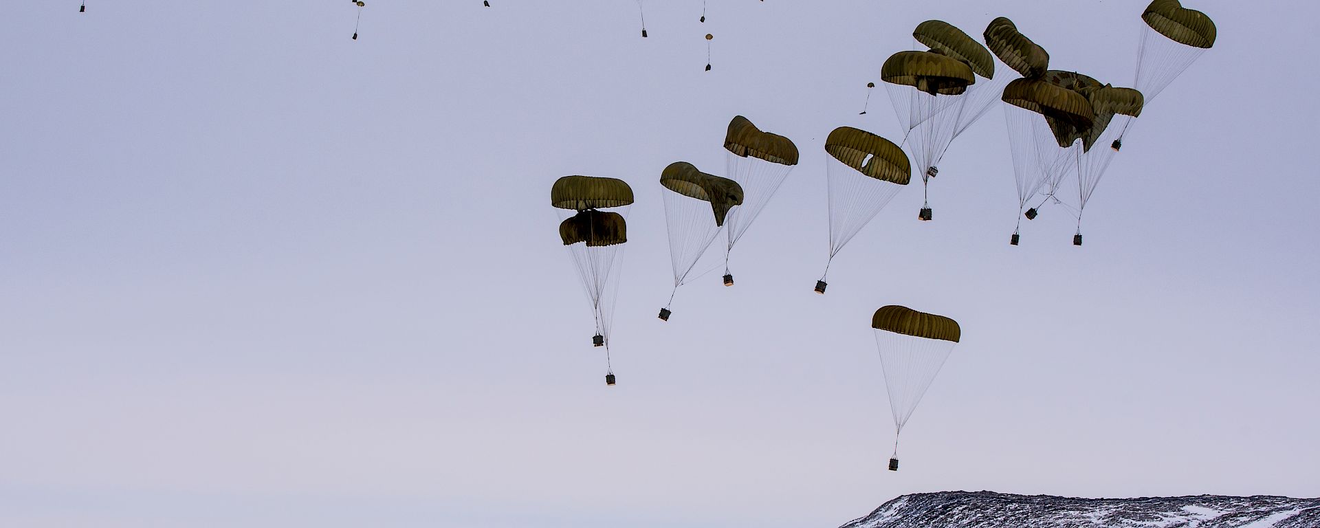 Parachutes above boxes of supplies falling towards the ice.