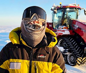 An expeditioner in the snow at Wilkins aerodrome wiht a tractor in the background