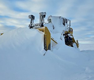 Dozer moving snow with blue sky scattered with clouds in the background