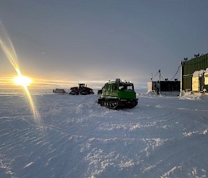 Sun setting with vehicles and buildings in the background at Wilkins aerodrome