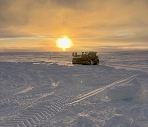 A dozer set against a setting sun on the vast ice and snow