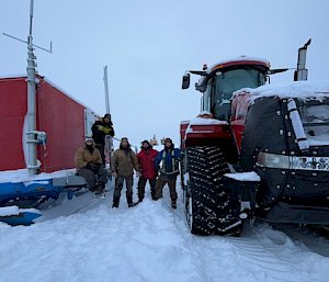 The Wilkins team standing in between a Quadtrac tractor and a red building at Wilkins aerodrome