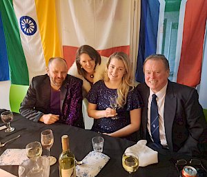 4 expeditioners sitting at a table with flags in the background at midwinter dinner