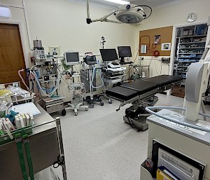 An operaying theatre with a bed in the middle, light overhead and various instruments and machines on trolleys around the edges of the room.