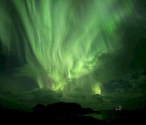A bright green aurora fills the night sky. There are lots of long vertical tendrils of green light.