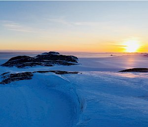 Photograph of sunset over the ice with rock in the background