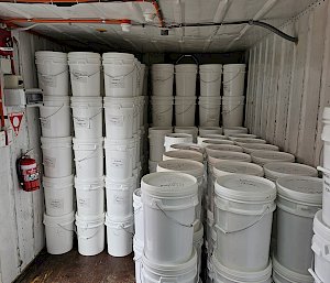 Lots of white, plastic buckets with lids, stacked on top of each other