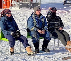Three expeditioners sitting on chairs on the ice playing a game called beer darts