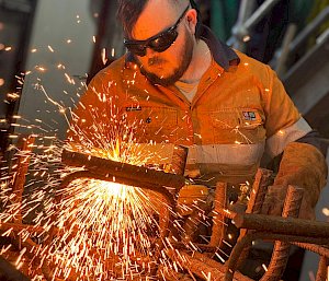 A man creating a steel bollard. Sparks are flying from the metal frame