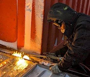 A man welds the edge of a steel container in sub-zero temperatures