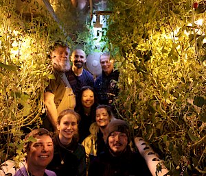 Eight expeditioners inside the hydroponics shed surrounded by plants.