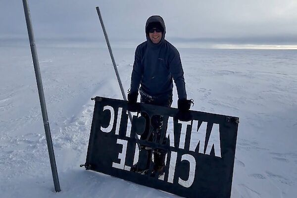 The old Antarctic Circle sign gets removed by an expeditioner standing next to the poles holding the sign standing on the ice