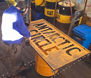 An expeditioner spray painting the Antarctic Circle sign yellow in the workshop