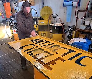 An expeditioner puts the finishing touches of yellow paint on an Antarctic Circle sign