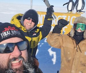 The three expeditioners standing in front of the sign celebrating finishing fixing the sign