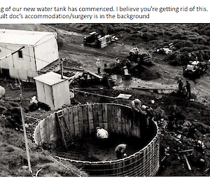 A black and white photo of a construction site including a round wooden watertank without a roof