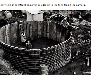 A black and white photo of people inside a wooden water tank under construction