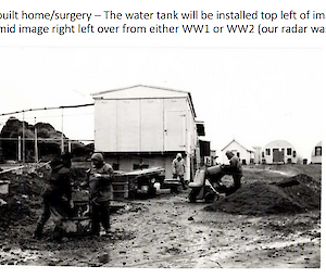 A black and white photo of people working a cement mixer on a building site at Macquaire Island. A semi-cylindrical Nissan hut is in the background.