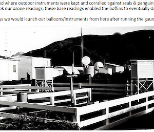 A black and white photo of a fenced yard with weather instruments inside.