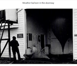 A black and white photo of two people and a weather balloon in a doorway