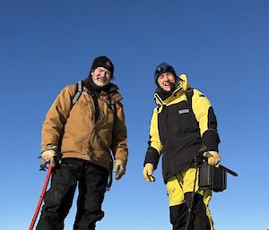Two people posing for a photo. The photo is taken from ground level looking up at them.