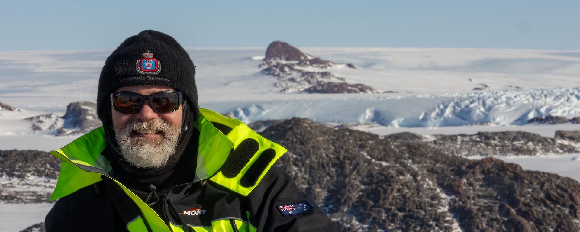 Dominik in a green jacket with mountain peaks and the Antarctic plateau behind