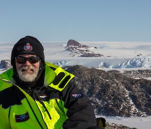 Dominik in a green jacket with mountain peaks and the Antarctic plateau behind