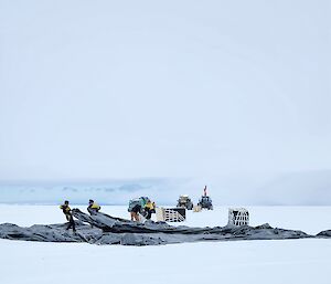 Four people hauling parachutes away from boxed cargo.