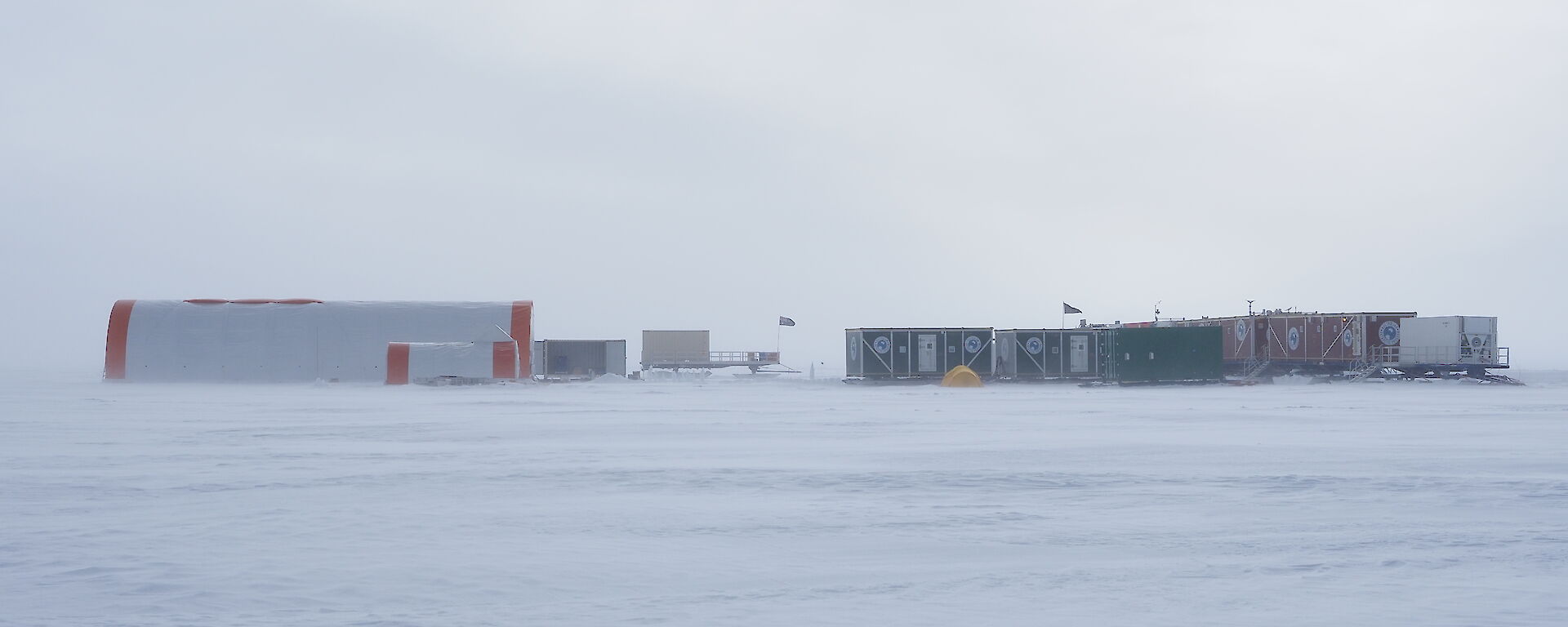 A large semi-cylindrical tent acting as a drilling shelter, erected next to a similar, smaller tent, alongside a line of shipping containers housing accommodation for Antarctic personnel