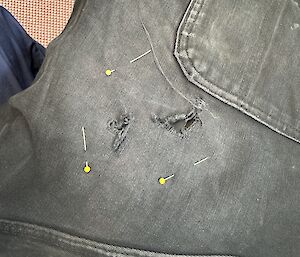 Three pins marking a hole in a pair of jeans