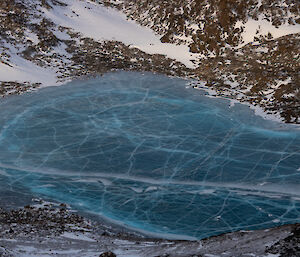 A blue frozen lake, it's surface covered in cracks, viewed from the air