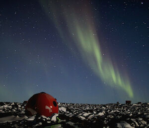 An aurora in sky with a red apple hut in the foreground
