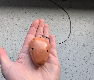 A small wooden object with small holes in it, is held in the palm of someone's hand