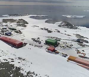 Aerial view of colourful rectangular buildings on snow-covered rocks, with a bay in the distance.