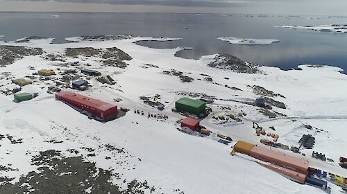 Aerial view of colourful rectangular buildings on snow-covered rocks, with a bay in the distance.