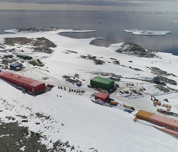 Aerial view of colourful rectangular buildings on snow-covered rocks, with a bay in the distance.