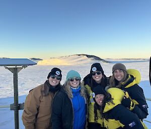 Five women standing in a close group on the deck of RSV Nuyina parked in sea ice